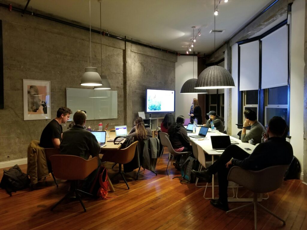 Diverse team collaborating in a modern office setting with laptops and presentation screen.